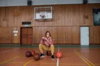A basketball player resting among basketballs on a gym floor