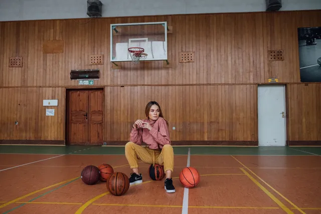 A basketball player resting among basketballs on a gym floor