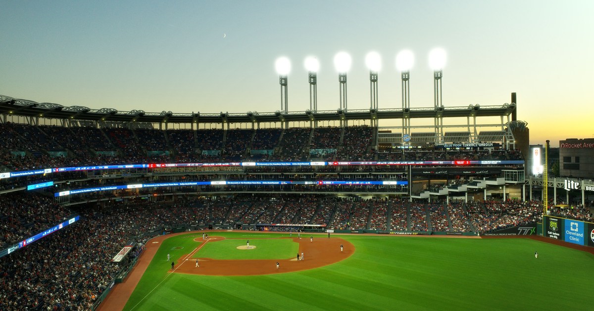 A baseball stadium under the lights at dusk, seen from the upper deck