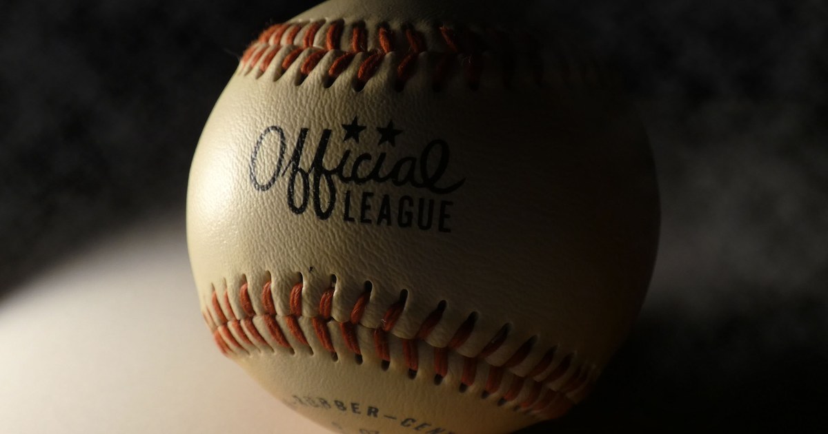 A close-up of an Official League baseball dramatically lit against a dark background