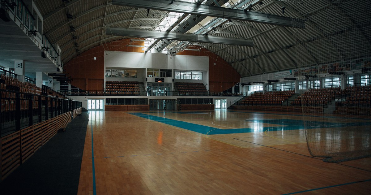 An empty indoor basketball arena with hardwood flooring and tiered seating