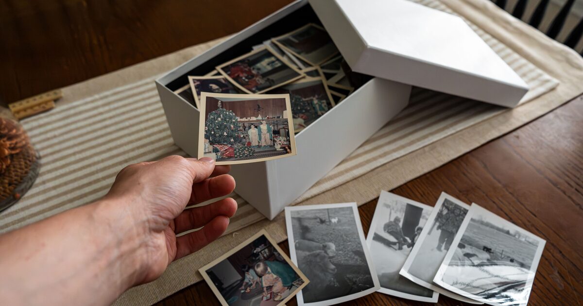 A hand lifting old photographs from a storage box of a nostalgic family collection