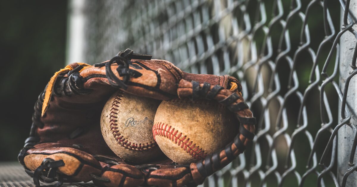 Two well-worn baseballs cradled in a leather glove beside a chain-link fence