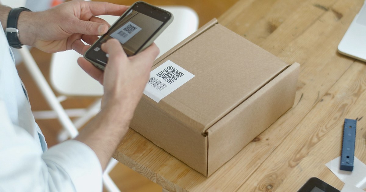 Hands using a smartphone to scan a printed code label on a parcel