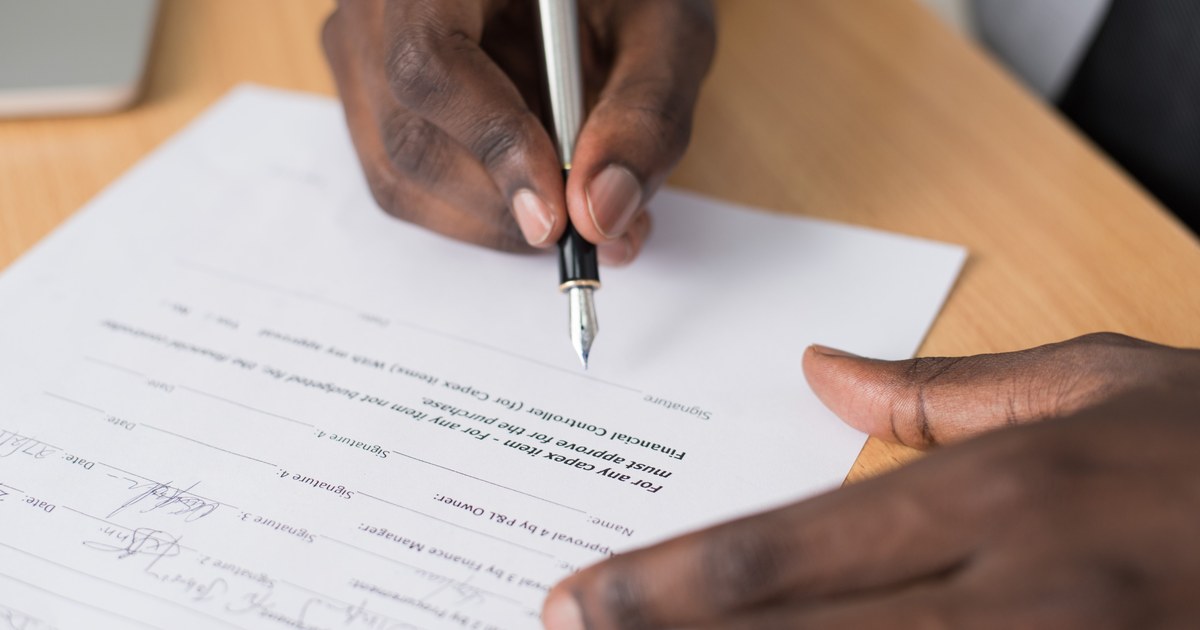 Close-up of hands signing a formal document with a fountain pen