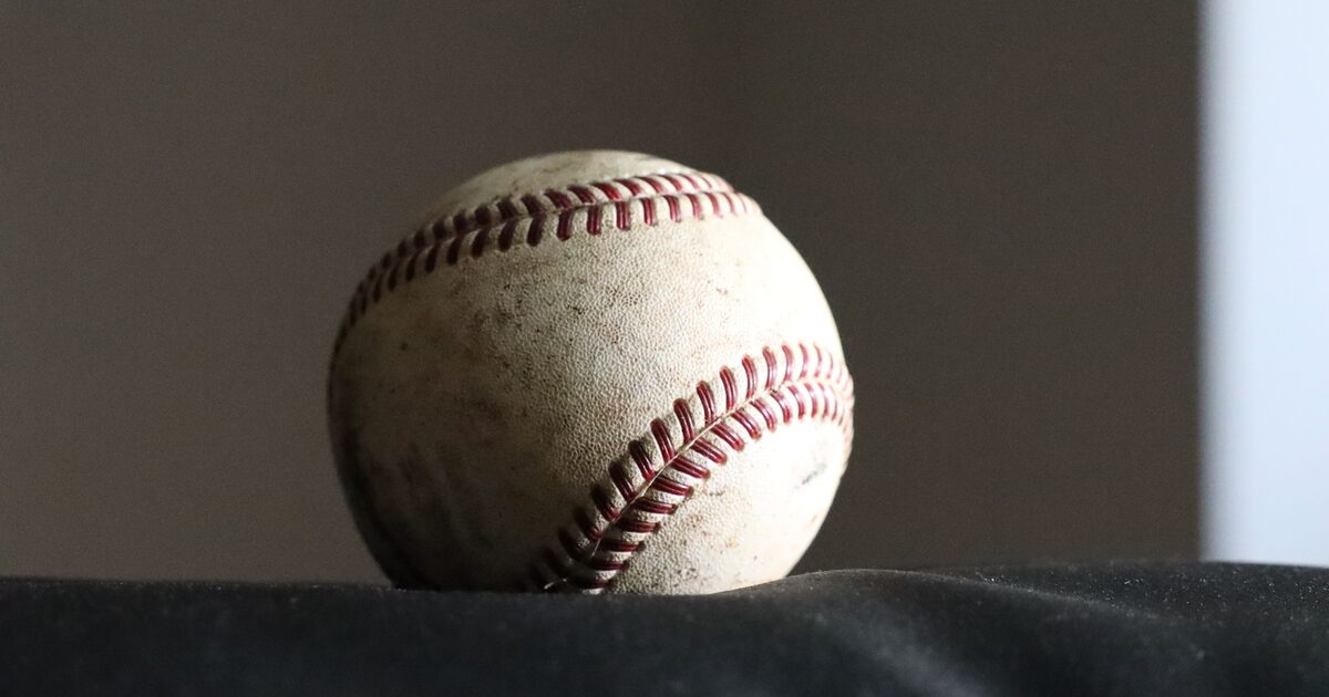 A single weathered baseball lit against a dark background, showing its aged stitching