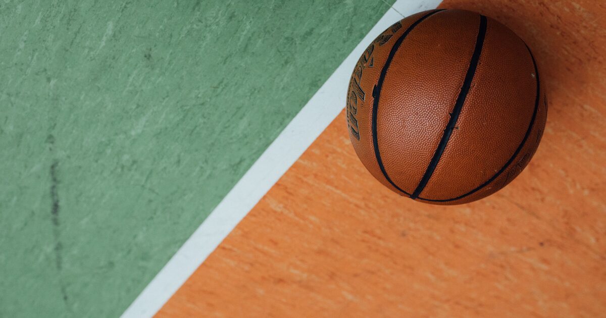 A basketball resting on a two-tone orange and green outdoor court