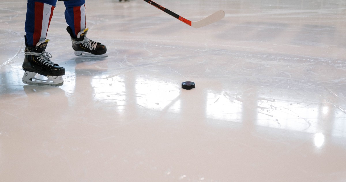 A hockey player's skates and stick beside a puck on reflective rink ice