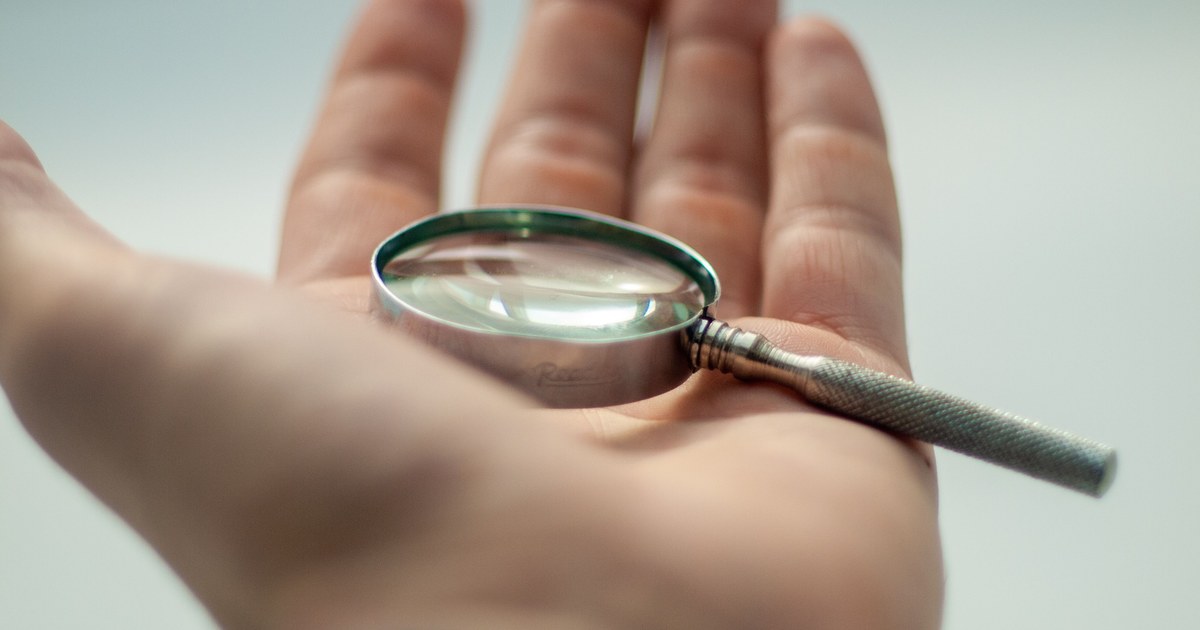 An open hand holding a small magnifying glass